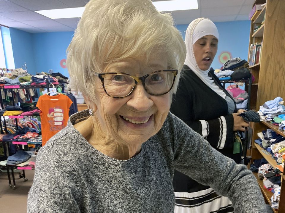 Volunteer smiling among racks of children's clothing at Kid's Kloset